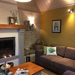 Gemuetliches Wohnzimmer des Ferienhauses Windekind mit Blick auf die Felder in De Panne, belgische Kueste, mit Kamin und gemuetlicher Sitzecke.