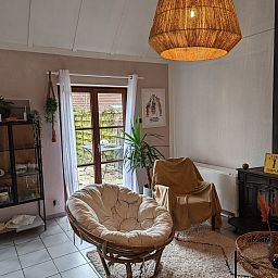 Gemuetliches Wohnzimmer des Ferienhauses Duinendaele II in De Panne, belgische Kueste, mit bequemen Stuehlen und einem gemuetlichen Holzofen.