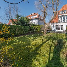 Ruime tuin van Appartement Jong & Blij 2 op de begane grond in De Haan, Belgische kust, ideaal voor ontspanning en genieten van de natuur.