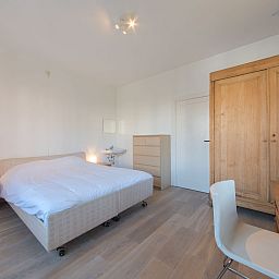 Slaapkamer in Appartement Jong & Blij 2 op de begane grond met tuin in De Haan, Belgische kust, met comfortabel bed en houten interieur.