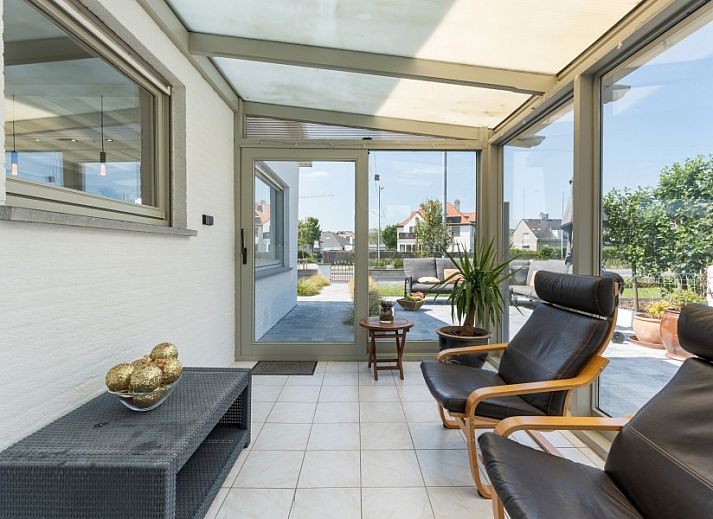 Stijlvolle woonkamer in Villa Renee, De Haan, Belgische kust, met leren banken en grote ramen.