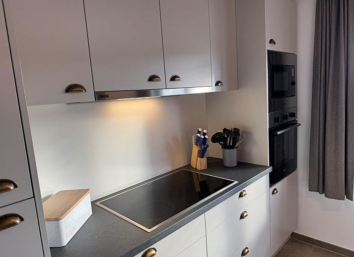 Gezellige eetkamer en keuken in vakantiehuis Westhinder II H23, Koksijde, West-Vlaanderen, met moderne inrichting en uitzicht op de tuin.