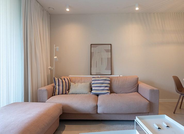 Gezellige woonkamer van West Bay vakantiehuis in Westende, West-Vlaanderen met comfortabele bank en uitzicht op de tuin.