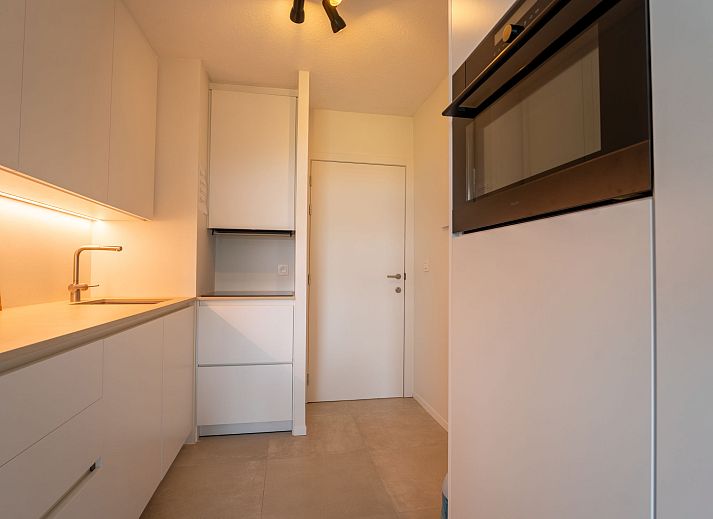 Moderne Kueche im Apartment Residentie Astrid in Bredene, Westflandern, Belgien, mit schlichten weissen Schraenken und stimmungsvoller Beleuchtung.