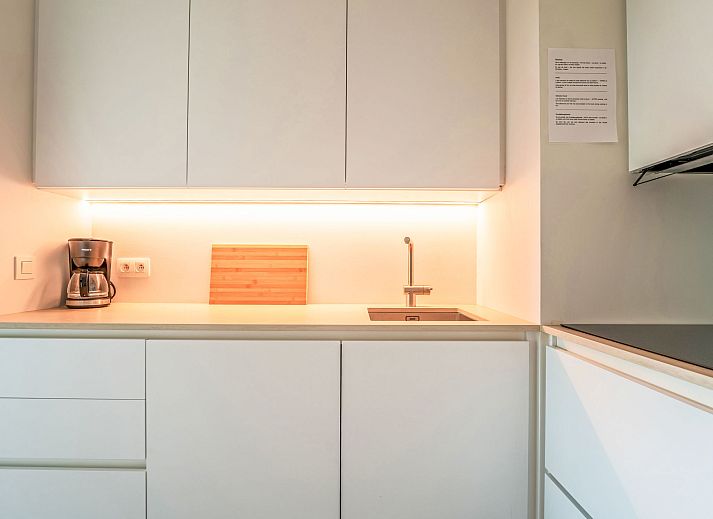 Moderne Kueche im Apartment Residentie Astrid in Bredene, Westflandern, Belgien, mit schlichten weissen Schraenken und stimmungsvoller Beleuchtung.