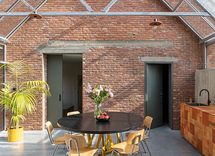 Heller Innenraum eines Ferienhauses in Sint-Pauwels, Belgien, mit Glasdach und gemuetlichem Essbereich.