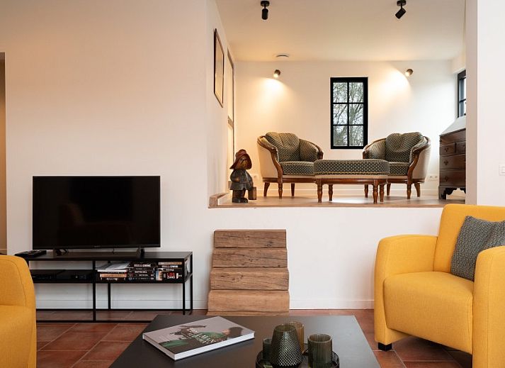 Gemuetliches Wohnzimmer von Mushoeve in Zoersel, Antwerpen mit Kamin und bequemen gelben Stuehlen.