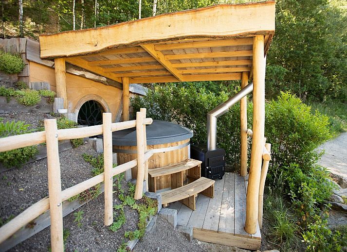 Hobbit House 1 in Neeroeteren, Limburg, Belgie, een uniek vakantiehuis met een rustieke veranda omringd door weelderige natuur.