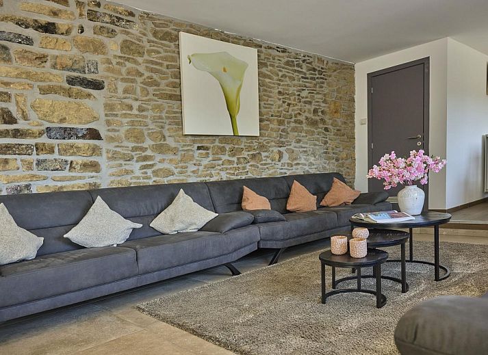 Gemuetliches Wohnzimmer im Ferienhaus "La Ferme" in Lierneux, Ardennen, mit bequemen Sofas und rustikalen Steinwaenden in Belgien.