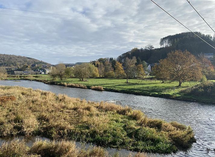 Gezellige binnenruimte van vakantiehuis Le Fournil in Manhay, Ardennen, met een rustieke houtkachel en authentieke stenen haard.