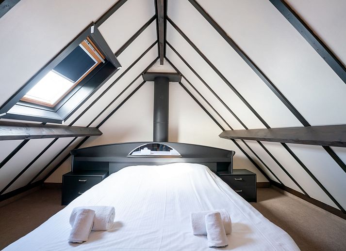 Sfeervolle slaapkamer in Vakantiehuis Zeewind II in Bredene, Belgische kust, met houten balken en zacht beddengoed voor een rustgevend verblijf.