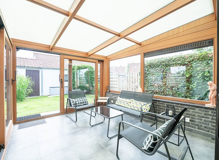 Gemuetliches Wohnzimmer des Ferienhauses Reynaertpark in Bredene, belgische Kueste, mit bequemen Sofas und Blick auf den Garten.