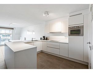 Moderne Kche im vierten Ferienhaus Delmar in Koksijde, Westflandern, Belgien, mit schlichter weier Oberflche und gerumigem Grundriss.