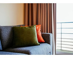 Gemtliche Sitzecke im vierten Ferienhaus Les Petrels, Koksijde, Westflandern, mit bunten Kissen und Blick auf den Balkon.