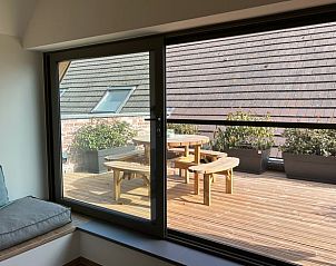 Gemtliche Terrasse beim Ferienhaus in Poperinge, Westflandern, Belgien, mit Holzsitzgelegenheiten und Blick auf die reizvolle Umgebung.