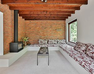 Gezellige woonkamer in Vakantiehuisje in Geel, Winkelomheide, met rustieke bakstenen muur en houtkachel, ideaal voor ontspanning.