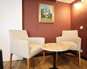 Gezellige zithoek in chalet Sous les Hetres, Robertville, Ardennen. Comfortabele fauteuils en kunst aan de muur creren een huiselijke sfeer.