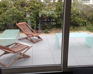 Terrace with deck chairs in bungalow in Oostduinkerke, Belgian coast, overlooking green garden.