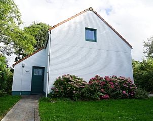 Front view of De Haan Cottage 670, charming vacation home in De Haan, Belgium, surrounded by greenery.